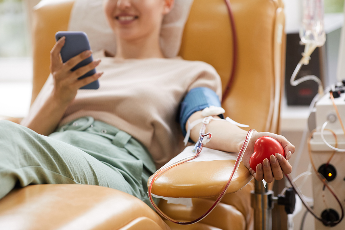 Close-up of young woman smiling and looking at her mobile phone while donating blood.