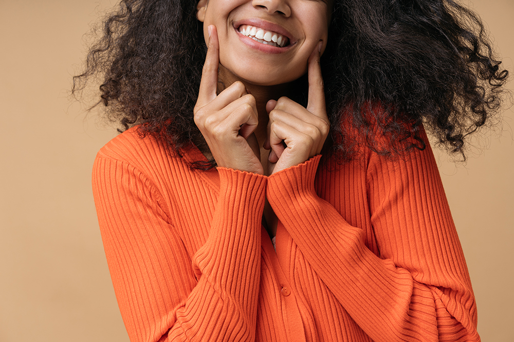 Close up portrait of young happy Black woman in an orange sweater showing off her healthy smile.