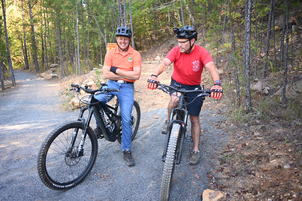Two men sit on mountain bikes on a mountain biking trail.